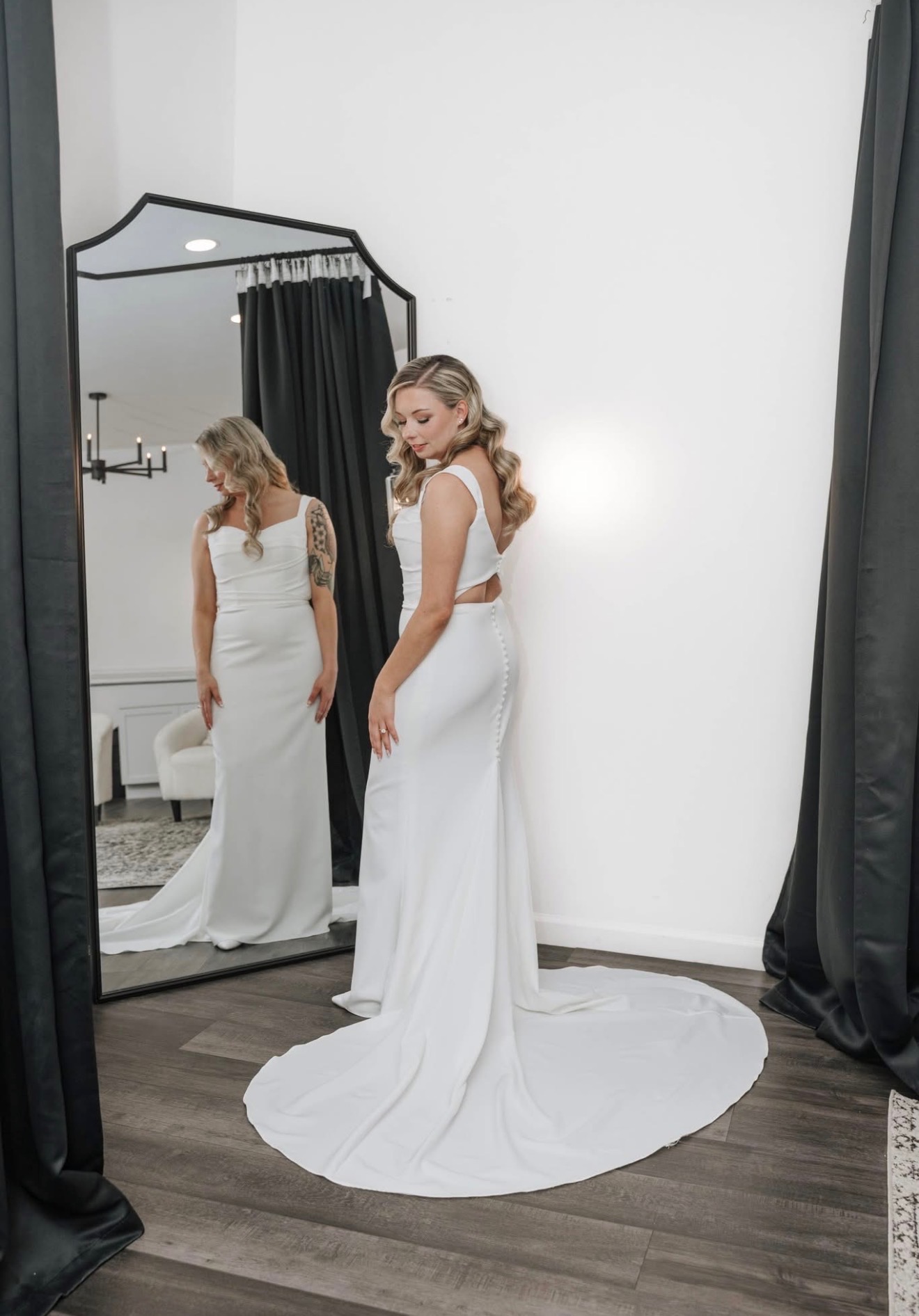 Bride in a sleek white gown with soft waves in front of a mirror
