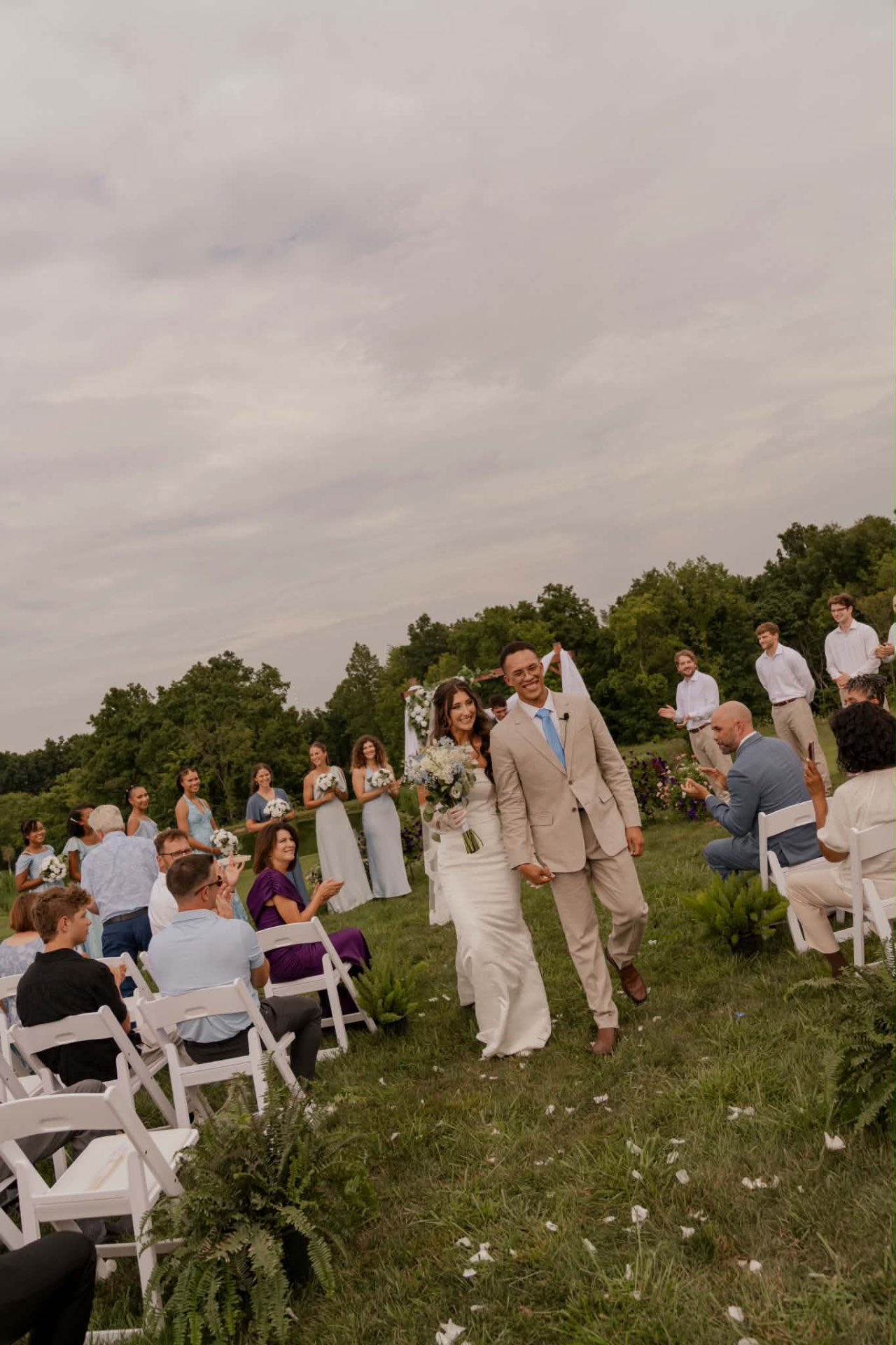 Bride and groom walking down the aisle past bridesmaids in light blue dresses with soft glam bridal makeup