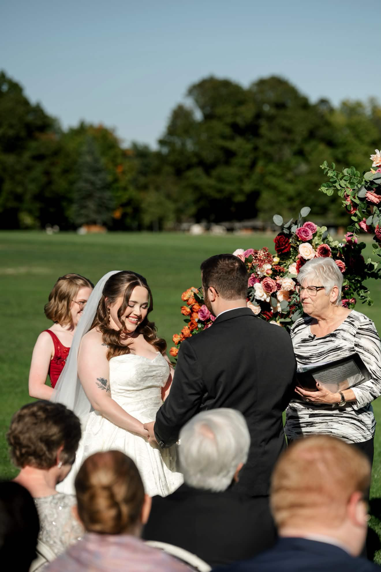 Bride in a strapless ivory gown and long veil holding hands with her groom during an outdoor lawn ceremony, soft glam bridal makeup