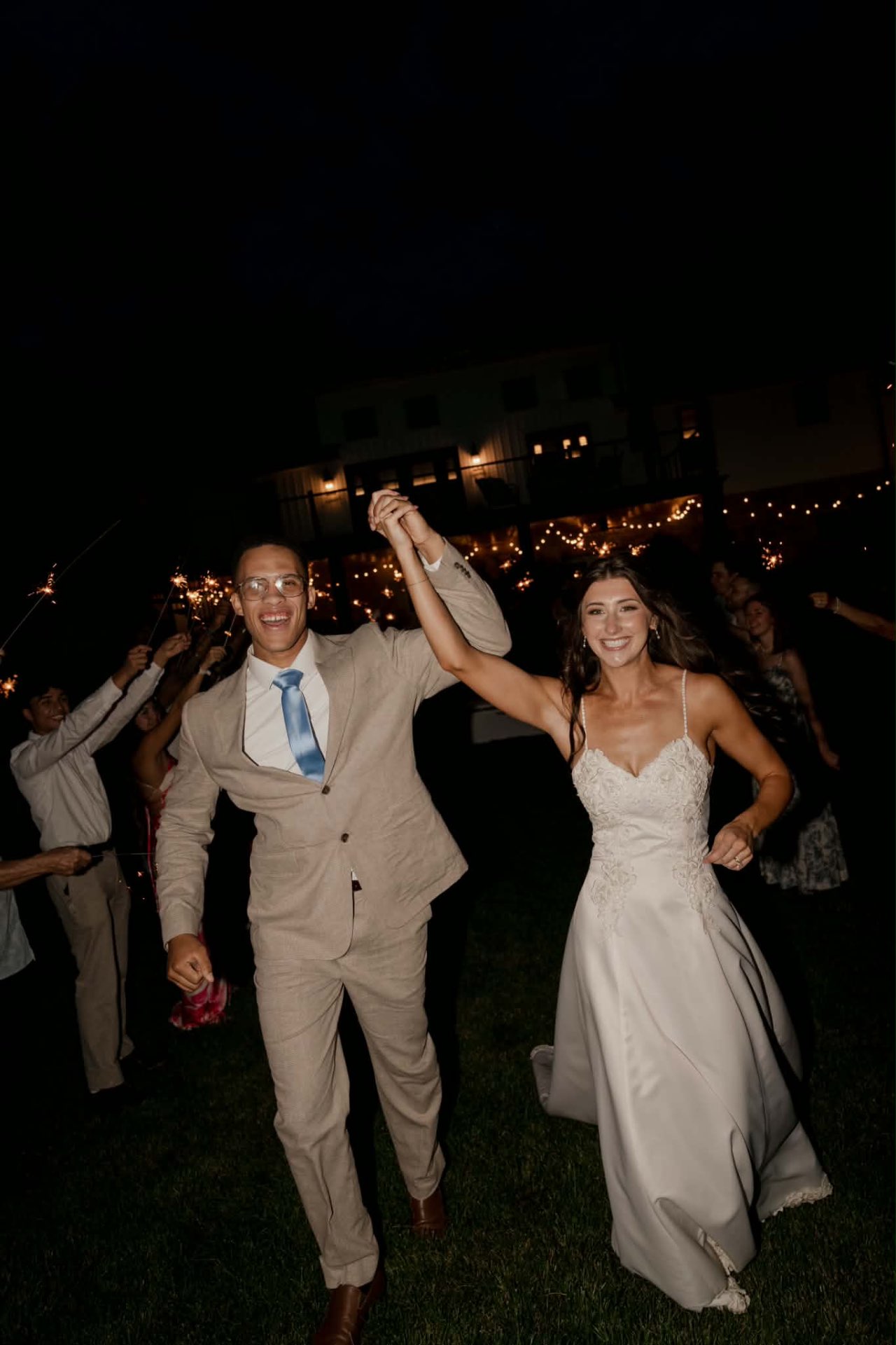 Bride and groom running through a sparkler send-off at night, bride in a white lace bodice gown